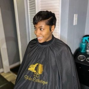 Jeune femme avec une coupe pixie courte noire et brillante, coiffée en finger waves élégantes, souriant au salon de coiffure