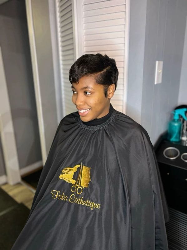 Jeune femme avec une coupe pixie courte noire et brillante, coiffée en finger waves élégantes, souriant au salon de coiffure
